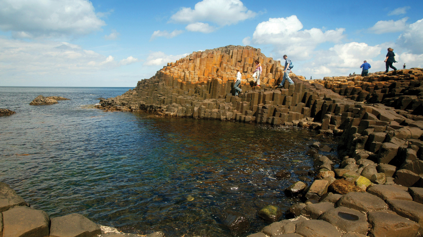 People climbing along the hexagonal formations arising out of the sea at Giants Causeway